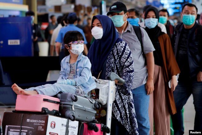 Seorang anak perempuan mengenakan masker bersama ibunya antre untuk pemeriksaan suhu tubuh di tengah penyebaran COVID-19 di Bandara Halim Perdanakusuma, Jakarta, 20 Maret 2020. (Foto: Reuters)