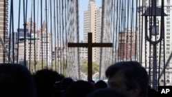 FILE - A replica cross rises above the crowd during a procession across the Brooklyn Bridge in New York, April 6, 2012. The Diocese of Brooklyn reached a $27.5 million settlement with four men who said they were sexually abused as boys.
