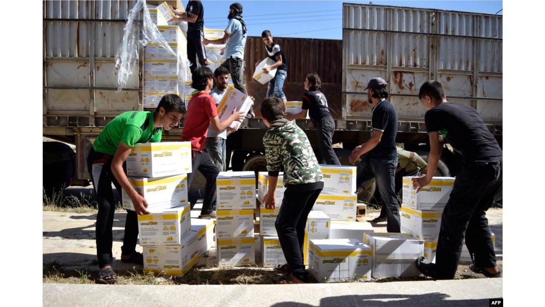 Syrian men carry aid parcels provided by the U.N. World Food Program (WFP) and the Syrian Arab Red Crescent in the rebel-held town of Al-Houla, on the northern outskirts of Homs in central Syria, on May 25, 2016.