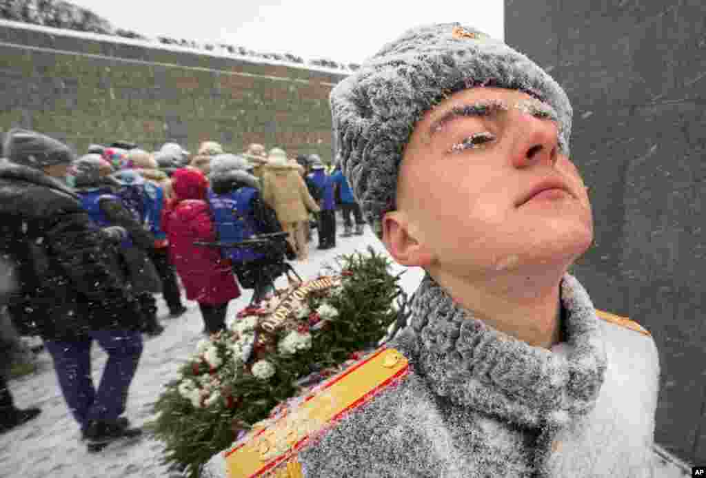 A Russian honor guard stands in snowfall as people walk to the Motherland monument to place flowers and wreaths at the Piskaryovskoye Cemetery where most of the Leningrad Siege victims were buried during World War II, in St. Petersburg, Russia.