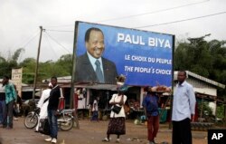 FILE - Residents wait for transportation under a campaign poster for Cameroon President Paul Biya in Doula, Cameroon, Oct. 6, 2011.