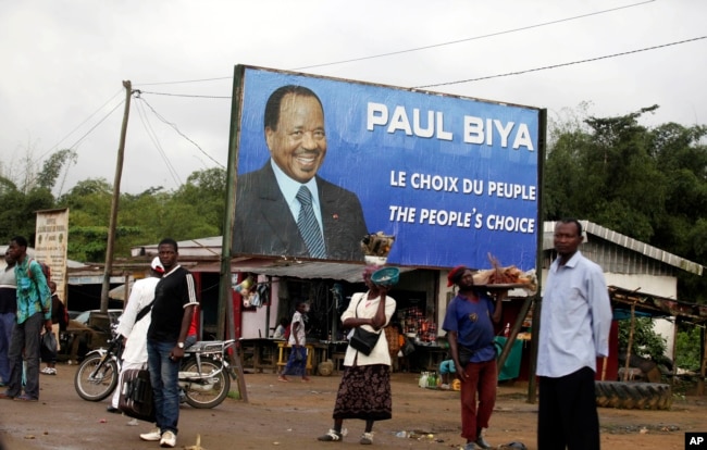 FILE - Residents wait for transportation under a campaign poster for Cameroon President Paul Biya in Doula, Cameroon, Oct. 6, 2011.