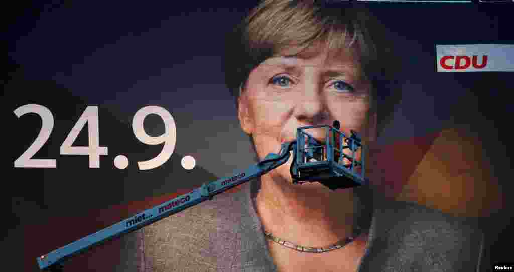 A crane operator steers his mobile crane next to a 18-metre wide 'Mega Poster' of Angela Merkel, German Chancellor and leader of the Christian Democratic Union party CDU, after fixing the lights for Merkel's campaign picture for the September 24 general e