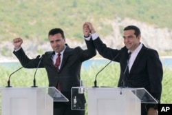 Greek Prime Minister Alexis Tsipras, right and his Macedonian counterpart Zoran Zaev, raise their hands during a signing agreement for Macedonia's new name in the village of Psarades, on June 17, 2018.