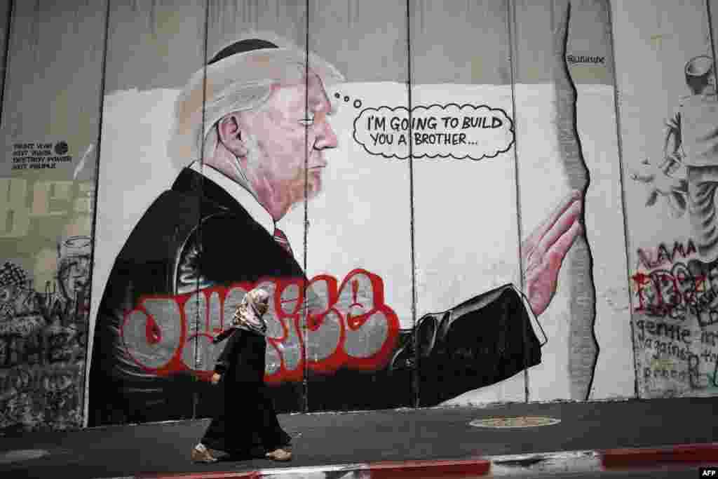 Seorang perempuan Palestina melewati lukisan graffiti berupa gambar Presiden AS Donald Trump dengan kopiah Yahudi di Bethlehem, Tepi Barat.