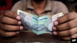 FILE - A cashier holds an Indian rupee. 