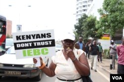 A Kenyan protester holds a sign cautioning against trusting the Independent Electoral Boundaries Commission, in Nairobi. (M. Yusuf/VOA)