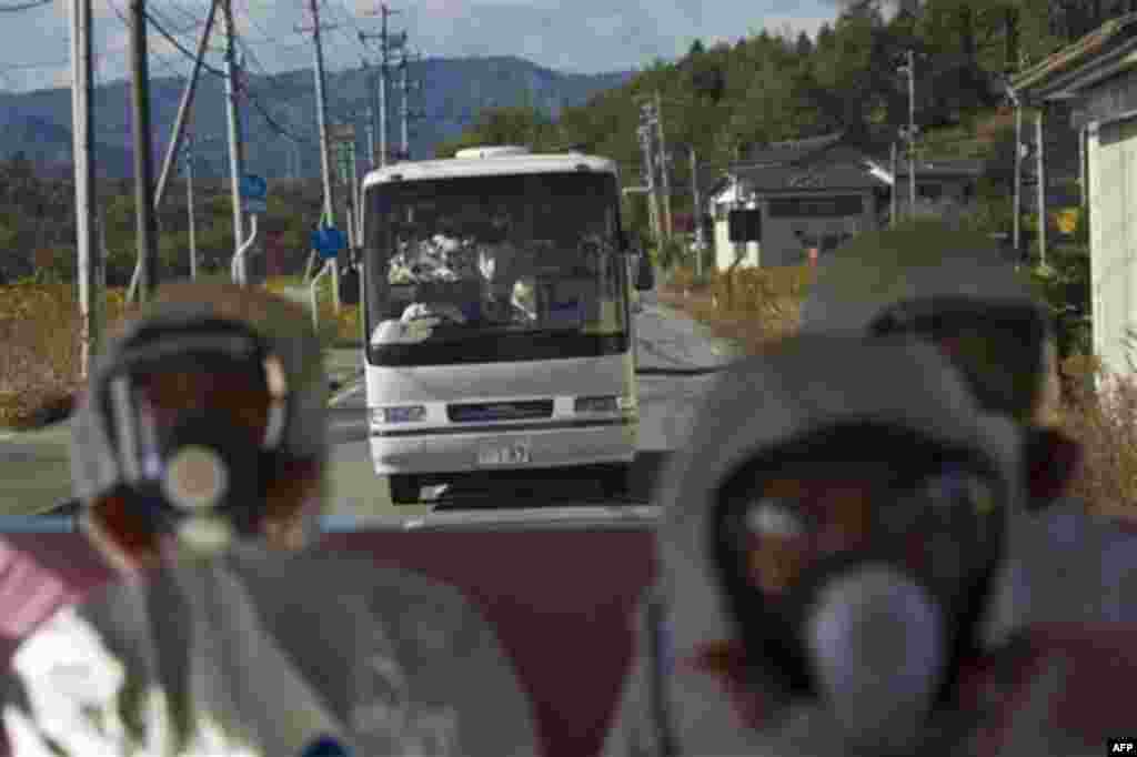 Japanese officials wearing protective suits and masks ride in the back of a bus while a second bus carrying officials and Japanese journalists follow as they drive through the contaminated exclusion zone on their way to the crippled Fukushima Dai-ichi nuc