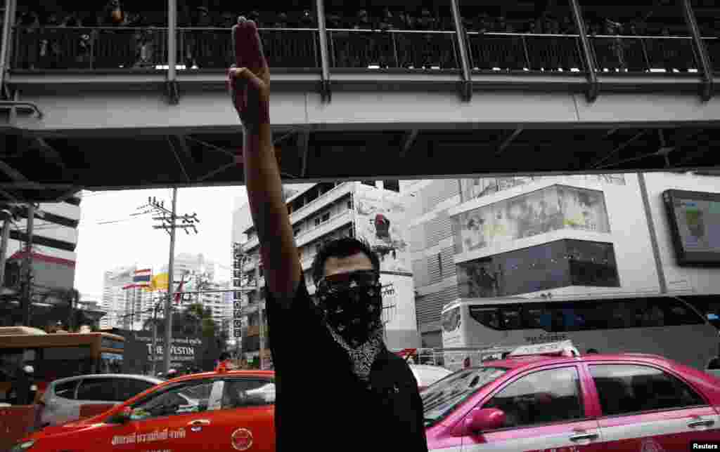 Seorang demonstran anti-kekuasaan militer mengangkat tiga jari tengah ke udara, diawasi oleh tentara dari jalan layang, dalam sebuah demonstrasi singkat di sebuah pusat perbelanjaan di Bangkok (1/6).