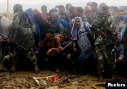 Macedonian policemen try to keep migrants and refugees under control before they cross the border line from Greece into Macedonia, near the Greek village of Idomeni, Sept. 10, 2015.