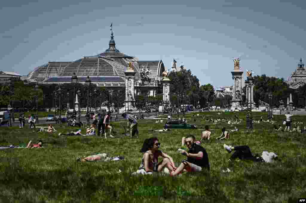 People enjoy a sunny day on a lawn near the Grand Palais and the Pont Alexandre III bridge in Paris as France partially lifted restrictions to prevent the spread of the COVID-19.