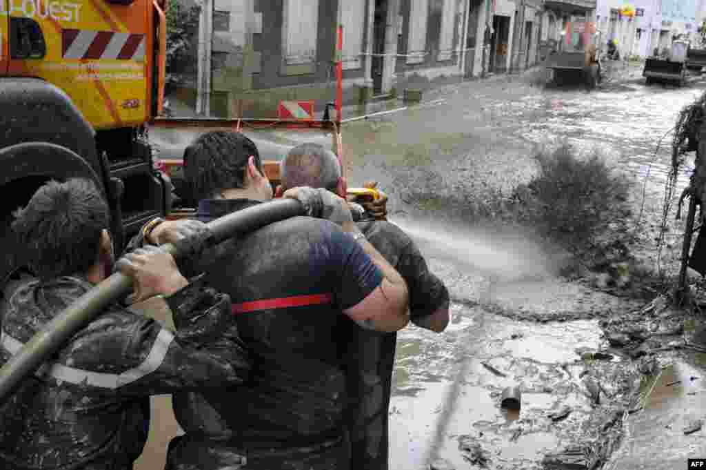 Petugas pemadam kebakaran menyemprotkan air di jalan yang tertutup lumpur di Saint-Beat, Perancis baratdaya, dalam operasi pembersihan setelah kawasan itu terendam banjir bandang selama dua hari.