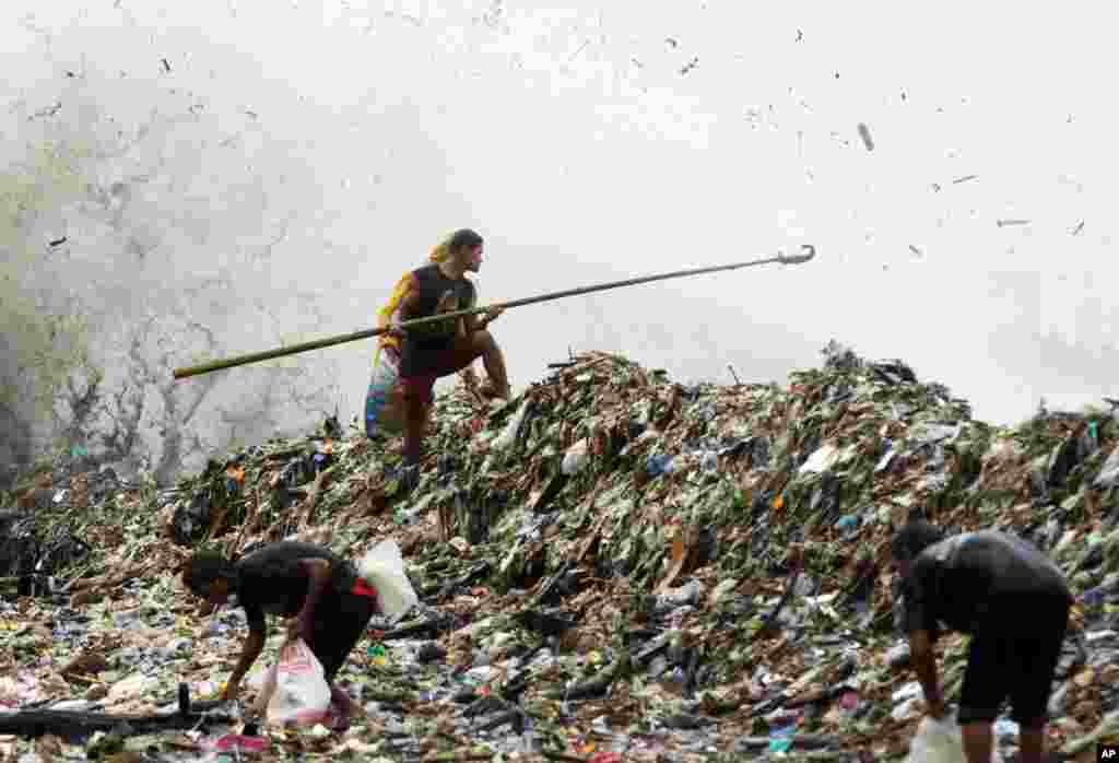 A man stands on a mound of garbage washed ashore by big waves as others search for recyclable materials, Aug. 1, 2012 along Roxas Blvd. in Manila, Philippines.