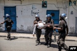 FILE- Comoros Gendarmerie officers carry an injured policeman wearing civilian clothes as they disperse opposition supporters, in Moroni, on March 25, 2019.
