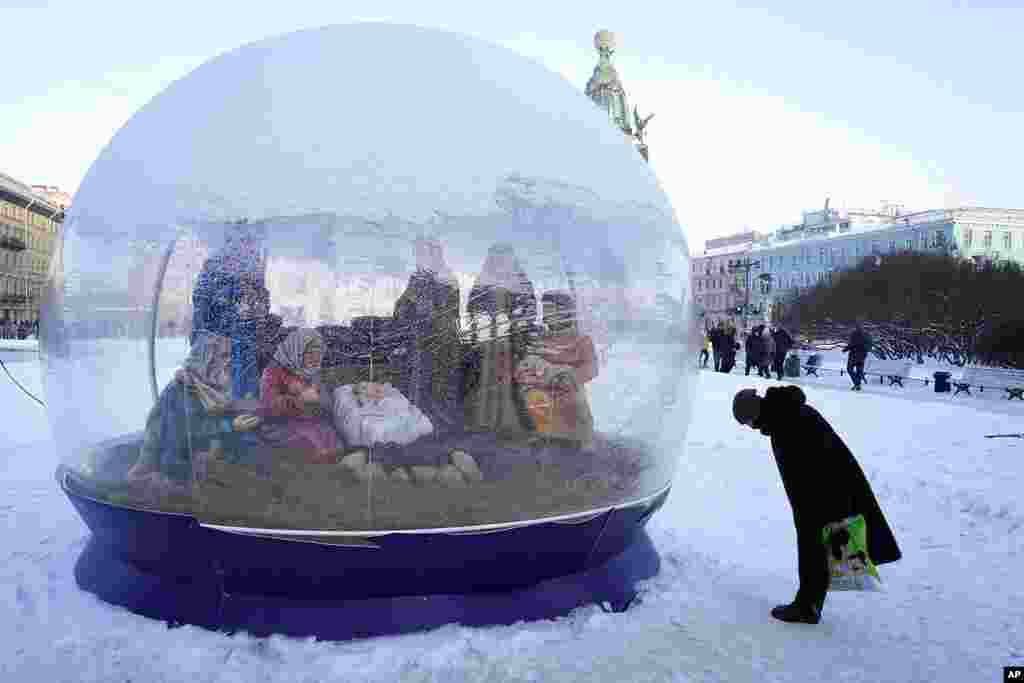 A woman bows to a giant nativity snow dome, near a church during Orthodox Christmas celebrations, in St. Petersburg, Russia.