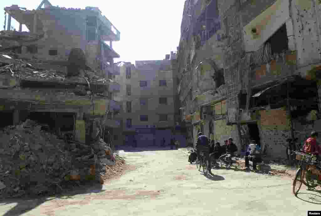Civilians sit near damaged buildings at the Palestinian refugee camp Yarmouk, south of Damascus, Feb. 12, 2014.