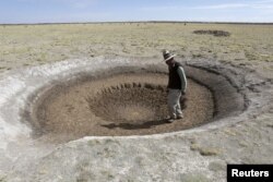 FILE - Farmer Sindulfo Fernandez inspects a dried watering hole for llamas in Orinoca, Oruro Department, Bolivia, Jan. 8, 2016. The water dried due to a drought.