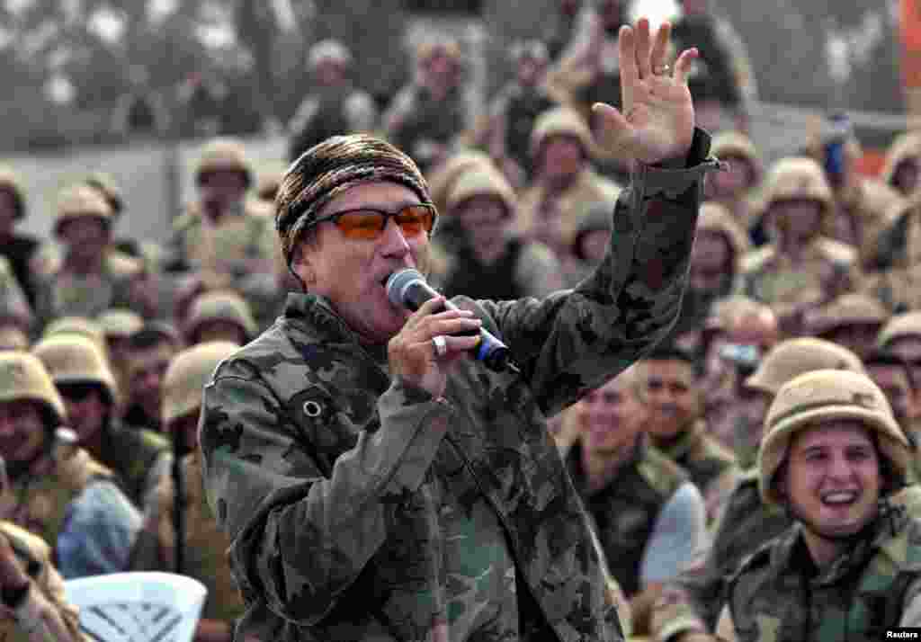 Comedian Robin Williams, wearing a camouflage jacket, entertains a cheering crowd of U.S. Army troops at Baghdad airport, Iraq, Dec. 16, 2003. 