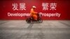 2015年7月15日北京市中心的一条街道上，一名维修工人骑着摩托车经过用中英文写着“发展”和“繁荣”的横幅