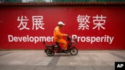 FILE - A maintenance worker rides a scooter past banners reading "Development" and "Prosperity" in English and Chinese on a street in central Beijing, July 15, 2015.