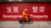 资料照：一名男子骑车路过北京市中心一堵宣传墙。（2015年7月15日）