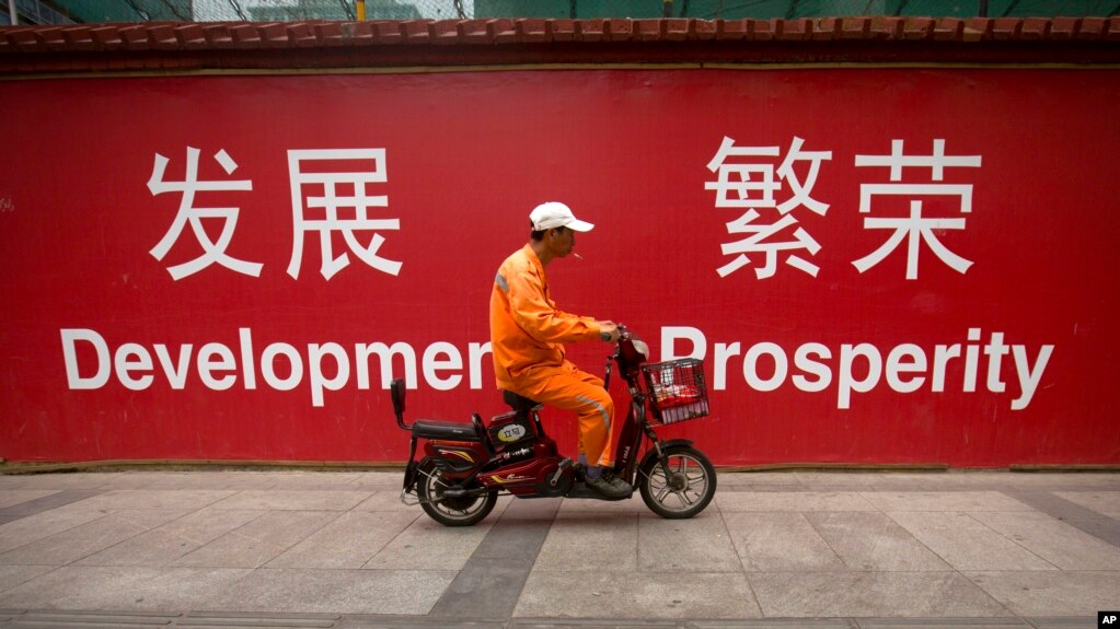 资料照：一名男子骑车路过北京市中心一堵宣传墙。（2015年7月15日）(photo:VOA)
