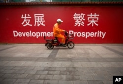 FILE - A maintenance worker rides a scooter past banners reading "Development" and "Prosperity" in English and Chinese on a street in central Beijing, July 15, 2015.