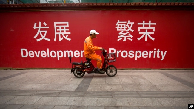 一名北京市清洁工人骑车经过市中心街头张贴的发展与繁荣的标语牌。(资料照片)
