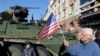 Чоловік тримає прапорець США біля американської броньованої машини Stryker з конвою військ НАТО під час зупинки для зустрічі з місцевими жителями в Білостоку, Польща. 24 березня 2015 р.