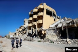 FILE - Youths walk past buildings that were destroyed during clashes between Libyan forces and Islamic State militants in Sirte, Libya, Nov. 1, 2017.