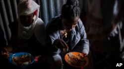 FILE - Displaced Tigrayan women, one wearing an Ethiopian Orthodox Christian cross, sit in a metal shack to eat food donated by local residents at a reception center for the internally displaced in Mekele, in the Tigray region of northern Ethiopia, on May