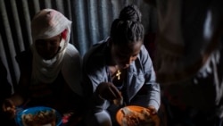 FILE - Displaced Tigrayan women, one wearing an Ethiopian Orthodox Christian cross, sit in a metal shack to eat food donated by local residents at a reception center for the internally displaced in Mekele, in the Tigray region of northern Ethiopia, on May 9, 2021.
