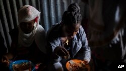 FILE - Displaced Tigrayan women sit in a metal shack to eat food donated by local residents at a reception center for the internally displaced in Mekele, in the Tigray region of northern Ethiopia, on May 9, 2021.