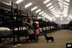 FILE - Verna Vasbinder prepares her new bunk in the city's new Temporary Bridge Shelter for the homeless as her dog, Lucy Lui, looks on in San Diego, Dec. 1, 2017.