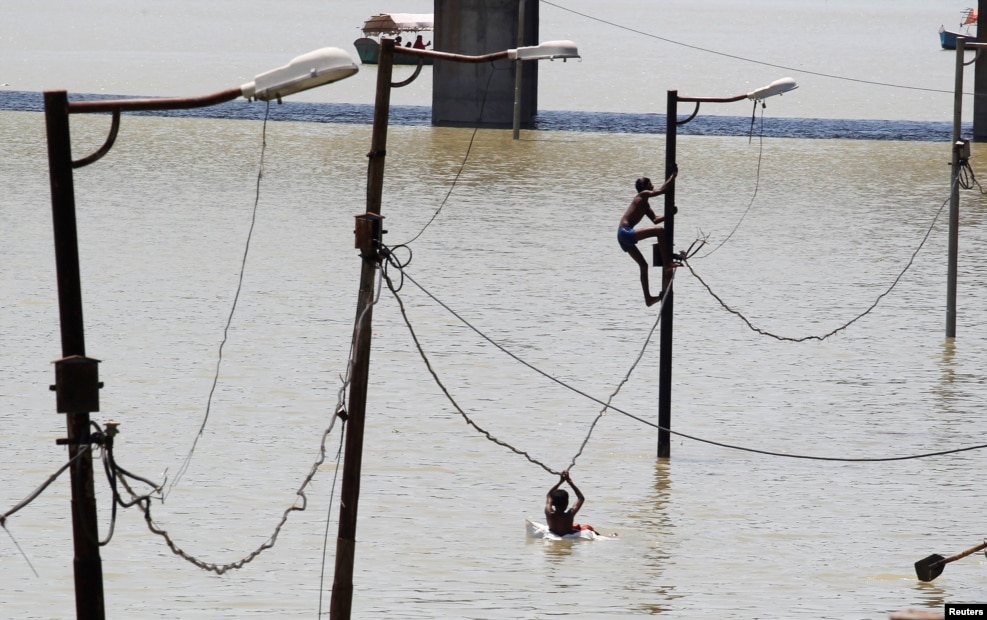 A boy climbs a partially submerged electric pole as he plays with others on the flooded banks of Ganga river, in Allahabad, India, Aug. 21, 2016.