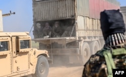 A truck carries men identified as Islamic State group fighters who surrendered to Kurdish-led Syrian Democratic Forces (SDF) as they are transported out of IS's last holdout of Baghuz, Syria, Feb. 20, 2019.