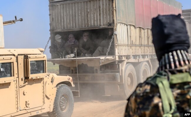FILE - A truck carries men identified as Islamic State group fighters who surrendered to Kurdish-led Syrian Democratic Forces as they are transported out of IS's last holdout of Baghuz, Syria, Feb. 20, 2019.