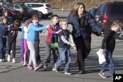 FILE - In this photo provided by the Newtown Bee, Connecticut State Police lead children from the Sandy Hook Elementary School in Newtown, Conn., following a reported shooting there, Dec. 14, 2012.