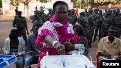 A woman casts her ballot at a polling station as soldiers watch in Bissau, April 13, 2014. 