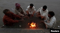 Fruit sellers sit around a fire to keep themselves warm during early morning hours along a road in Karachi December 30, 2013. 