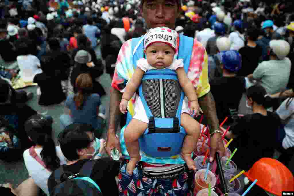 A vendor carrying a baby sells cool drinks during a protest in Bangkok, Thailand.