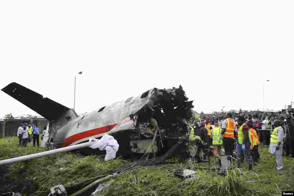 Rescue workers stand near the tail of a plane at the site of a crash near the Lagos international airport, Nigeria. Fifteen people were killed when an Embraer passenger plane crashed shortly after take-off just outside the airport's domestic terminal, authorities said.