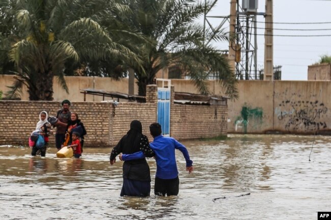 An Iranian family walks through a flooded street in a village around the city of Ahvaz, in Iran's Khuzestan province, on March 31, 2019.