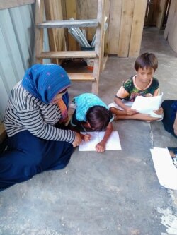 Dua orang anak yang sedang belajar dibimbing oleh guru yang mendatangi rumah mereka di desa Lende Tovea, Kecamatan Sirenja, Donggala, Sulawesi Tengah. (Foto: Save The Children Indonesia)