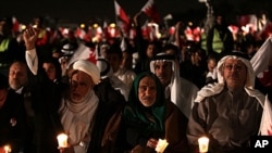 Bahraini opposition leaders Hamza al-Dairi, second left raising his fist, and Jalal Fairooz, right, holding a candle and Bahraini flag, both former opposition lawmakers from al-Wefaq society, participate in a rally in the eastern village of Sitra, Januar