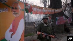 Tentara paramiliter berjaga-jaga di stadion kriket Sheri Kashmir tempat Perdana Menteri Narendra Modi, dengan posternya di kiri, dijadwalkan berpidato Senin (8/12) di Srinagar. (AP/Dar Yasin)