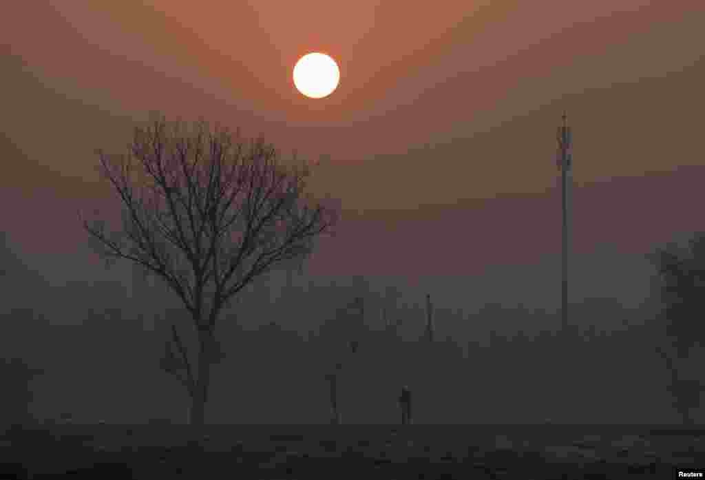 A man walks during sunrise in smog on a polluted day as a red alert issued for air pollution in Beijing, China.