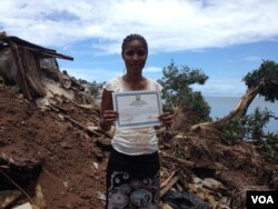 Juliana Sesay holds up her Ebola survivor discharge certificate as she stands in the place where her house and business were once located, in Freetown, Sierra Leone, Sept. 14, 2015. (N. Devries/VOA).