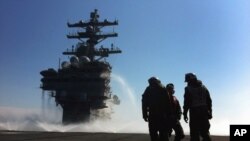 FILE - U.S. Navy deck crew stand near the island on the deck sprayed for radioactive decontamination aboard USS Ronald Reagan off the Japanese coast.