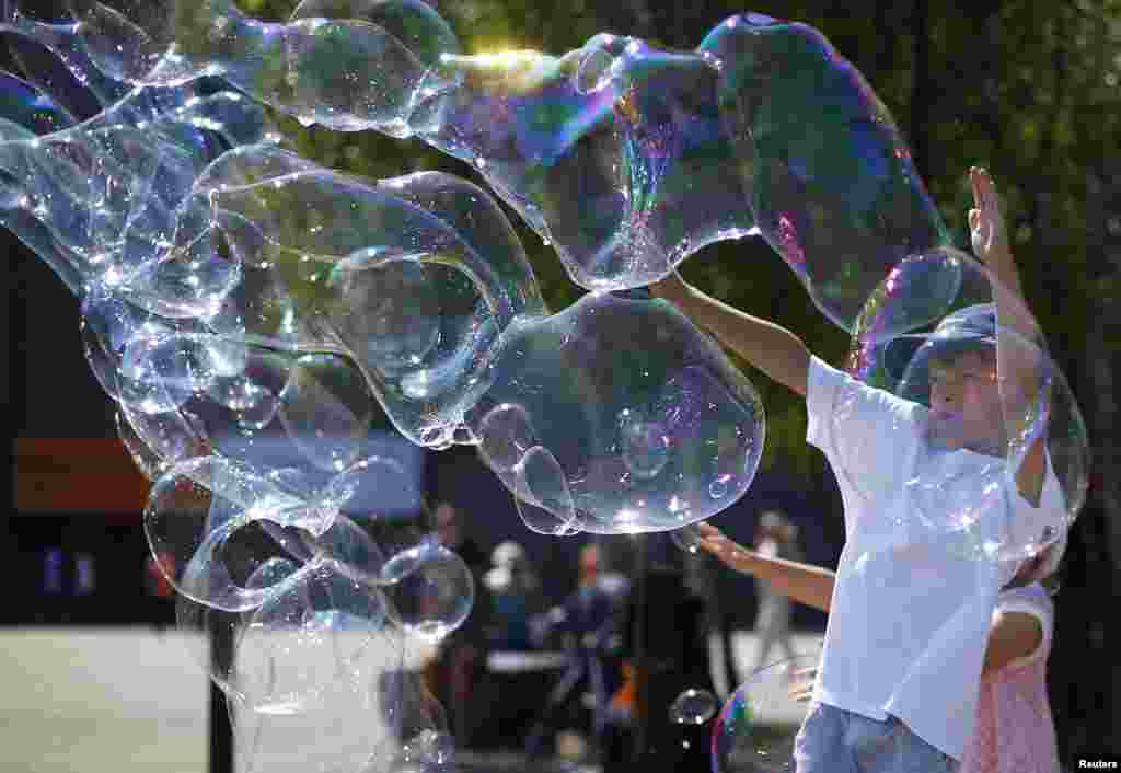 Children play with soap bubbles made by a busker on the South Bank on a hot day in central London.
